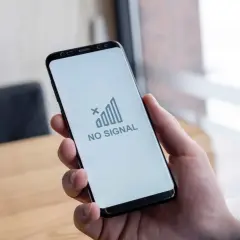 Dłoń trzyma smartfon z komunikatem "NO SIGNAL". Brak sieci w telefonie uniemożliwia kontakt.