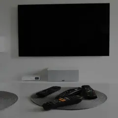 Na stole leżą piloty, a czarny ekran telewizora sugeruje, że jest brak obrazu w telewizorze.