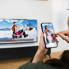 Oglądanie filmu z telefonu na TV przez WiFi. Dzieci zjeżdżają na sankach na ekranie telewizora i smartfona.