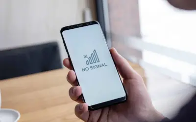 Dłoń trzyma smartfon z komunikatem "NO SIGNAL". Brak sieci w telefonie uniemożliwia kontakt.