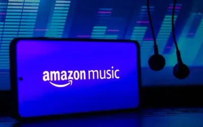 Słuchawki wiszą obok smartfona z logo Amazon Music. Tło to niebieski equalizer, sugerujący muzyczną przygodę z Amazon Music Polska.