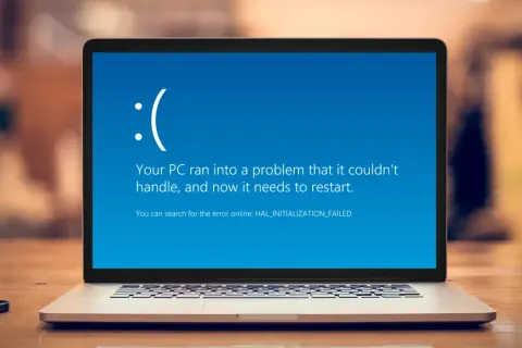 Laptop z niebieskim ekranem błędu Windows, smutną buźką i komunikatem "Your PC ran into a problem".