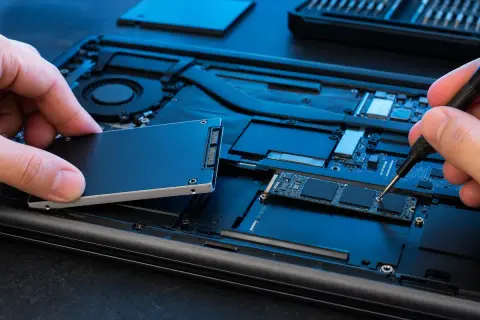 Wymiana dysku w laptopie: ręka trzyma nowy dysk SSD, druga dokręca śrubkę precyzyjnym śrubokrętem.