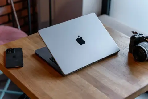 Srebrny MacBook z logo Apple, obok iPhone i aparat. Potężny procesor arm64 zapewnia płynność pracy.
