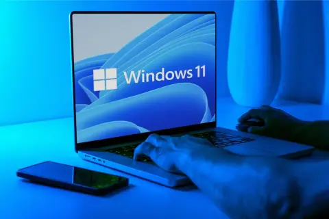 Ręce na klawiaturze laptopa z logo Windows 11. Dowiedz się, jak wejść do BIOS-u w Windows 11.