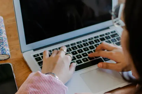 Kobieta pisze na laptopie. Obok leży telefon i notatnik. To jest print screen z jej pracy.