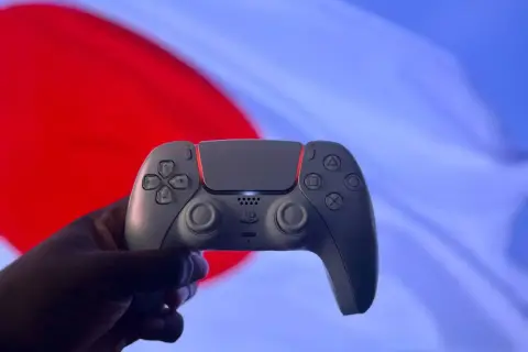 Dłoń trzyma biały kontroler DualSense. Czy gry z PS4 działają na PS5? Tak, większość z nich!