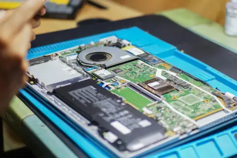 Rozłożony laptop na niebieskiej macie. Widać baterię, wentylator i zieloną płytę główną. Chcesz wiedzieć, jak sprawdzić jaką mam płytę główną?