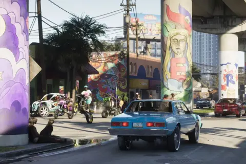 Kolorowe murale zdobią filary wiaduktu. W tle widać ulicę z samochodami i motocyklami, co może sugerować zbliżającą się premierę GTA 6.