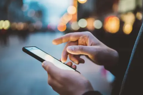 Dłonie trzymają smartfon, na ekranie którego widać rozmyte światła miasta. Szybki internet, jak APN Plus, pozwala na płynne przeglądanie.