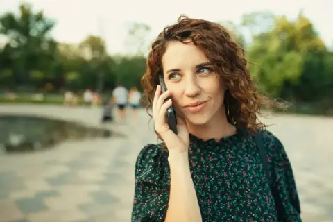 Kobieta z kręconymi włosami rozmawia przez telefon, zastanawiając się, jak odsłuchać pocztę głosową plus.