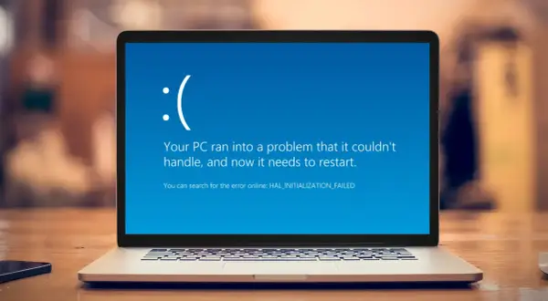 Laptop z niebieskim ekranem błędu Windows, smutną buźką i komunikatem "Your PC ran into a problem".