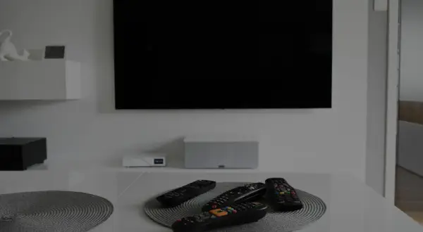 Na stole leżą piloty, a czarny ekran telewizora sugeruje, że jest brak obrazu w telewizorze.