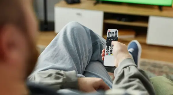 Osoba z pilotem w ręku, zastanawia się, kto nie musi płacić abonamentu RTV, oglądając zielony ekran telewizora.