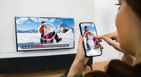 Oglądanie filmu z telefonu na TV przez WiFi. Dzieci zjeżdżają na sankach na ekranie telewizora i smartfona.