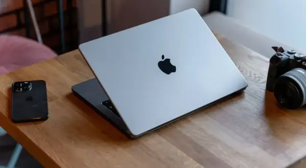 Srebrny MacBook z logo Apple, obok iPhone i aparat. Potężny procesor arm64 zapewnia płynność pracy.