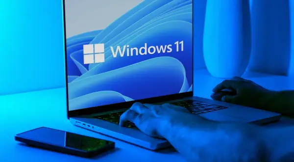 Ręce na klawiaturze laptopa z logo Windows 11. Dowiedz się, jak wejść do BIOS-u w Windows 11.