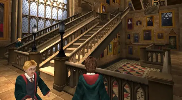 Dwóch uczniów w szatach Gryffindoru przemierza korytarz Hogwartu, jak w grach Harry Potter. Obok schodów wiszą ruchome portrety.