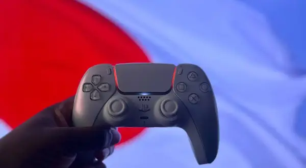 Dłoń trzyma biały kontroler DualSense. Czy gry z PS4 działają na PS5? Tak, większość z nich!
