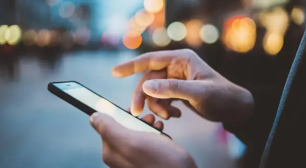 Dłonie trzymają smartfon, na ekranie którego widać rozmyte światła miasta. Szybki internet, jak APN Plus, pozwala na płynne przeglądanie.