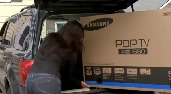 Kobieta wkłada do bagażnika samochodu duże pudło z telewizorem Samsung PDP TV.