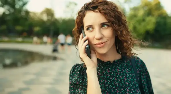Kobieta z kręconymi włosami rozmawia przez telefon, zastanawiając się, jak odsłuchać pocztę głosową plus.