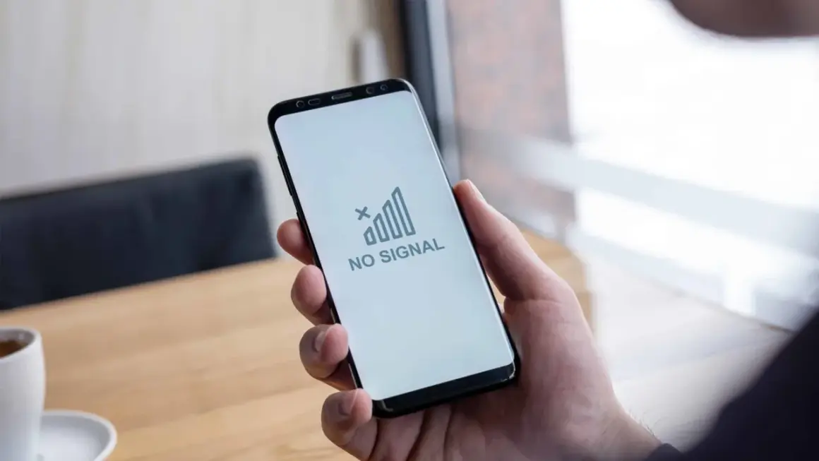 Dłoń trzyma smartfon z komunikatem "NO SIGNAL". Brak sieci w telefonie uniemożliwia kontakt.