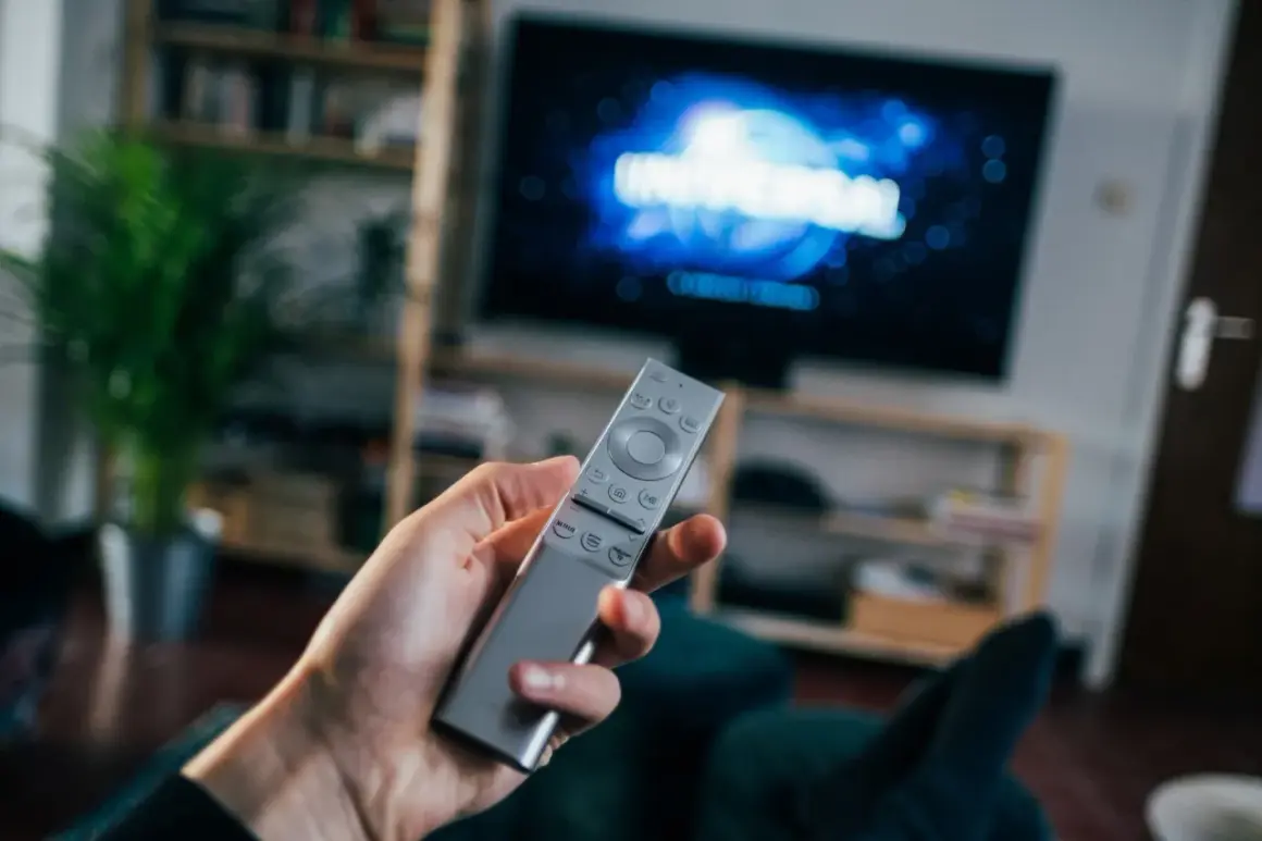 Dłoń trzyma pilota do telewizora, na ekranie logo Universal. Czas na seans filmowy z DVB-T.