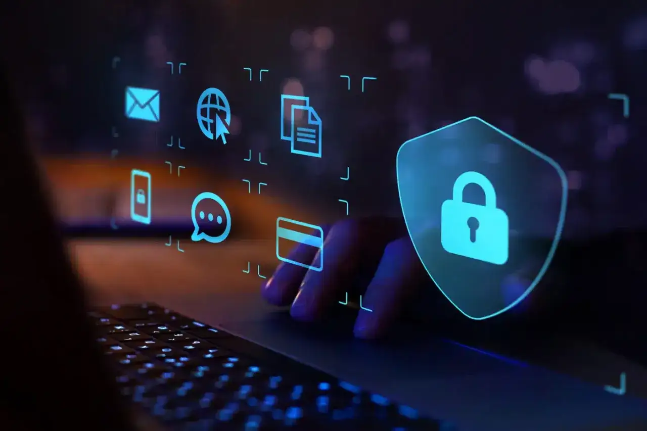 Dłoń na klawiaturze, ikony symbolizujące bezpieczeństwo danych, pocztę, internet i komunikację. Tarcza z kłódką, symbol ochrony przed antimalware.