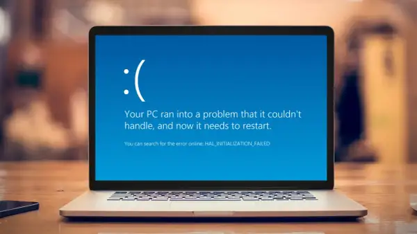 Laptop z niebieskim ekranem błędu Windows, smutną buźką i komunikatem "Your PC ran into a problem".