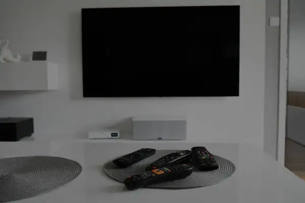 Na stole leżą piloty, a czarny ekran telewizora sugeruje, że jest brak obrazu w telewizorze.