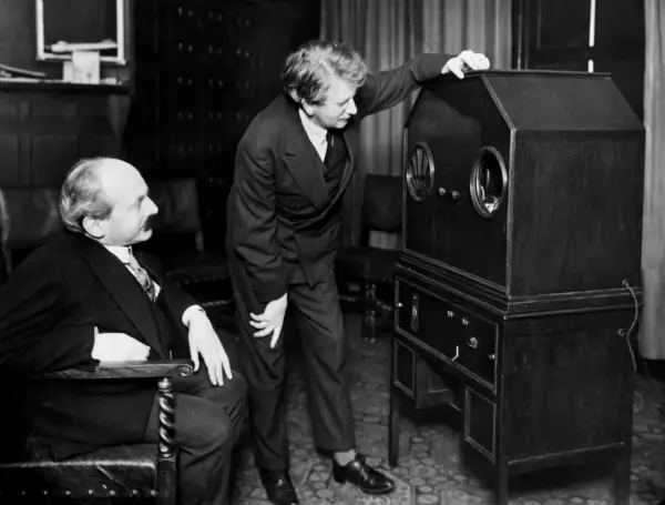Dwóch mężczyzn przy pierwszym telewizorze. Jeden siedzi, drugi stoi i dotyka obudowy.