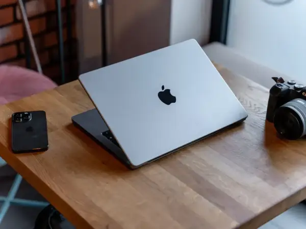 Srebrny MacBook z logo Apple, obok iPhone i aparat. Potężny procesor arm64 zapewnia płynność pracy.