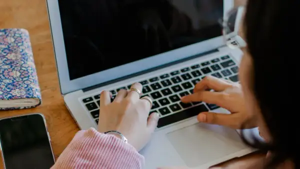 Kobieta pisze na laptopie. Obok leży telefon i notatnik. To jest print screen z jej pracy.