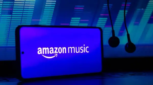 Słuchawki wiszą obok smartfona z logo Amazon Music. Tło to niebieski equalizer, sugerujący muzyczną przygodę z Amazon Music Polska.
