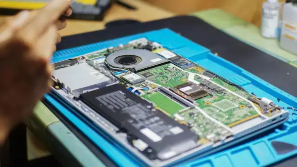 Rozłożony laptop na niebieskiej macie. Widać baterię, wentylator i zieloną płytę główną. Chcesz wiedzieć, jak sprawdzić jaką mam płytę główną?